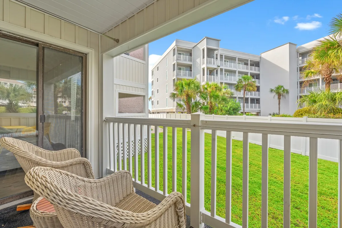 This inviting exterior scene showcases a balcony with wicker chairs overlooking a green lawn. The setup suggests a comfortable space for relaxing, enjoying a morning coffee, or socializing while taking in sunrise views, afternoon shade, or gathering in the evening. The balcony is framed by a railing, and the overall atmosphere is peaceful and welcoming, aligning with the off-season tranquility described in the section.