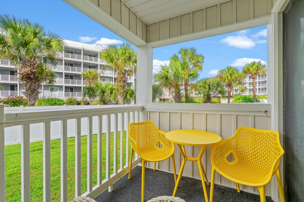 A cheerful and relaxed balcony scene with bright yellow chairs and a small round table, set against a backdrop of palm trees. The space feels perfect for enjoying morning coffee, reading, or simply soaking up the mild winter sun, highlighting the connection between indoor comfort and the outdoors even in the cooler months.
