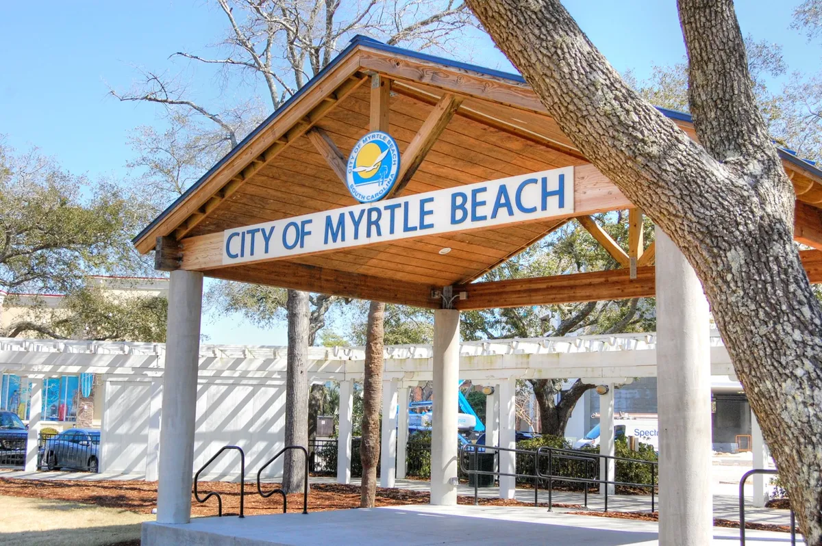 An exterior image featuring the 'CITY OF MYRTLE BEACH' signage on a charming wooden structure, surrounded by trees. The inviting scene suggests a friendly public space, ideal for exploring local events, cuisine, or festivals—even in winter.