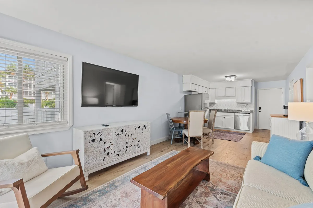 A close-up view of a comfortable sofa with a blue accent pillow, a stylish wooden coffee table, a decorative storage unit, and a television, with the dining area subtly visible in the background. The scene radiates comfort and is ideal for cozy evenings.