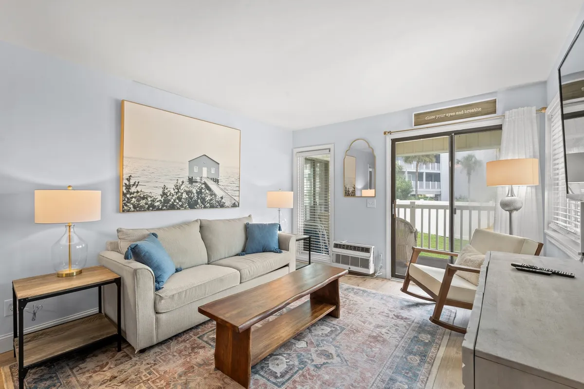 The hero image showcases a cozy living area with a comfortable sofa, a stylish coffee table, large artwork adding a touch of personality, and soft natural light streaming in through the window. The inviting setup suggests a space perfect for relaxing after a day at the beach, enjoying a good book, or gathering with family and friends for games and conversation.
