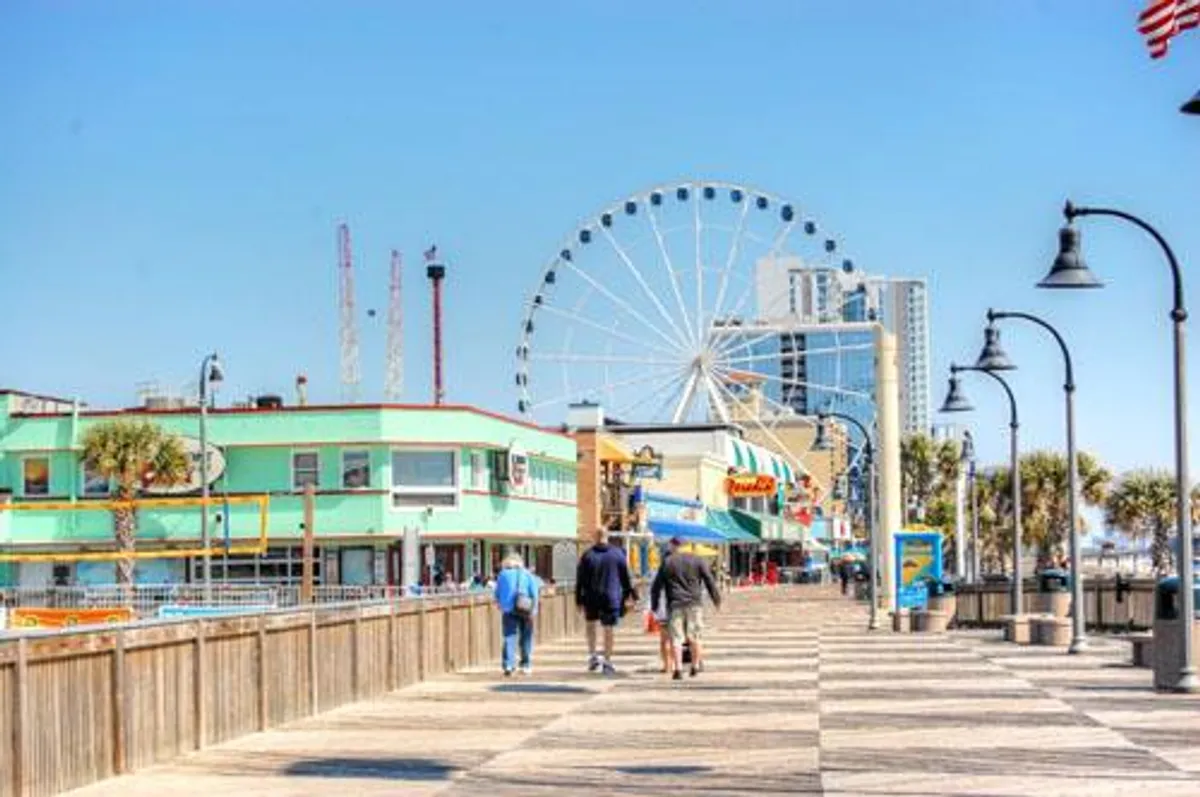 The lively Myrtle Beach boardwalk scene with a prominent ferris wheel, vibrant storefronts, and families enjoying the attractions. The joyful atmosphere captures the excitement of local adventures and making memories together.