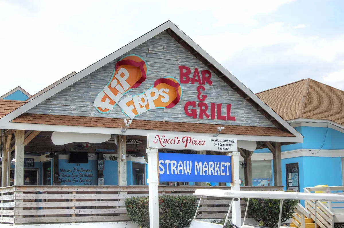 A vibrant exterior scene features signage for Flip Flops Bar & Grill, Nucci's Pizza, and Straw Market. The area bustles with energy, promising dining, socializing, and live events just moments from the property.